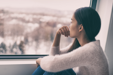 young woman with seasonal depression staring out window at snow-covered landscape