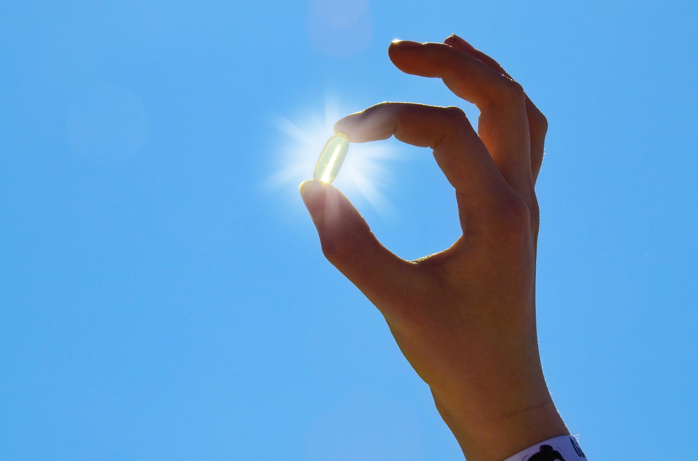 hand holding vitamin D pill against sun in blue sky