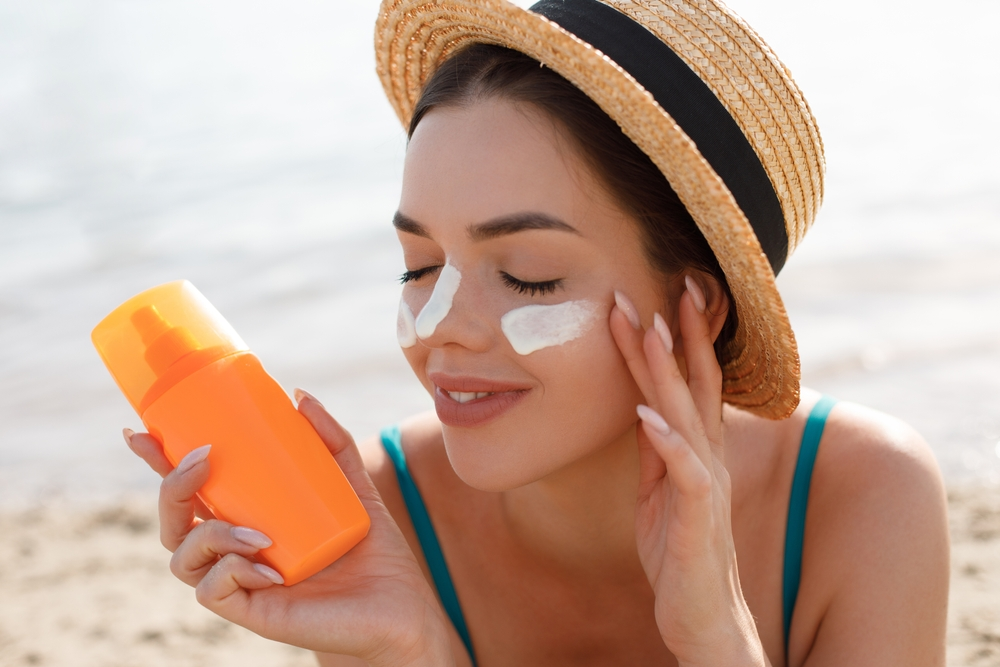 woman applying sunscreen to face while at the beach