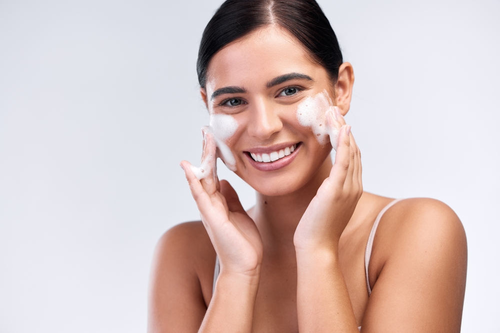 smiling woman washing face with foam cleanser