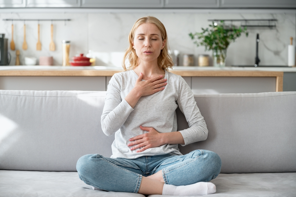 woman doing deep breathing exercising while sitting cross-legged on couch