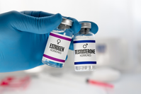 gloved hand holding two vials labeled Estrogen Hormones and Testosterone Hormones