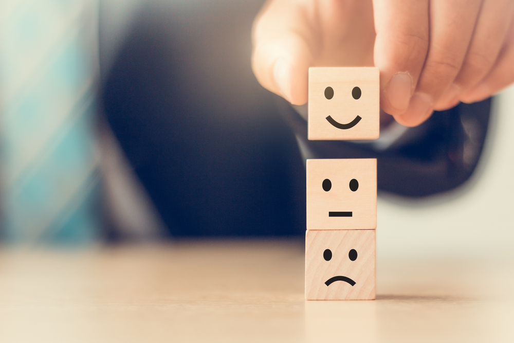 hand stacking 3 blocks with frowning, neutral, and smiling faces to show improving mental health