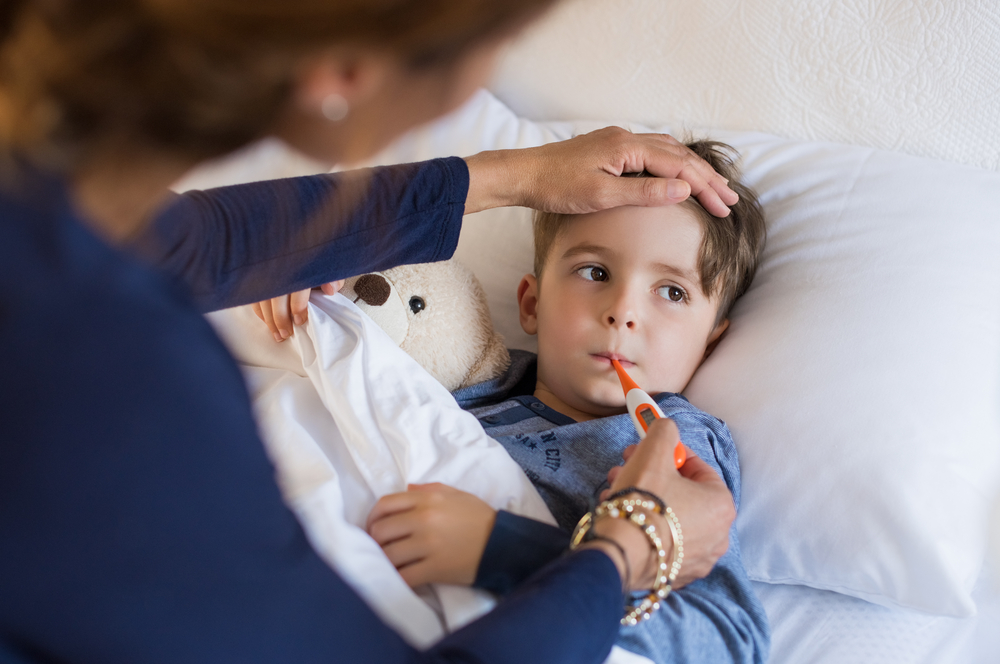 mother checking sick boy's temperature with thermometer and hand on his forehead